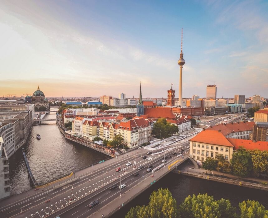 Vue aérienne de Berlin au coucher du soleil montrant la rivière Spree, des bâtiments aux toits rouges, des routes animées remplies de cyclistes, la tour de télévision de Berlin et la cathédrale de Berlin, avec la ligne d'horizon de la ville en arrière-plan. - Ekilib