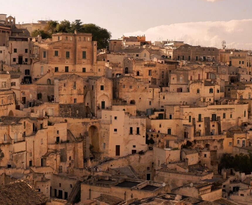 Une ville à flanc de colline, densément peuplée, avec des bâtiments en pierre beige de tailles et de hauteurs différentes, des toits plats et en tuiles, de petites fenêtres et des rues étroites - une toile de fond idéale pour explorer les pouilles à vélo sous un ciel partiellement nuageux. - Ekilib