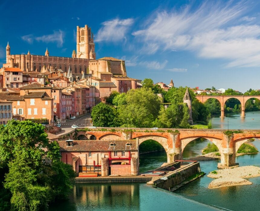 Vue d'Albi, France, avec la cathédrale d'Albi en briques rouges sur une colline, des bâtiments historiques et des ponts en arc sur le Tarn. Parfait pour les voyageurs explorant de Bordeaux à Toulouse le long de la route cycliste du Canal de Garonne. - Ekilib