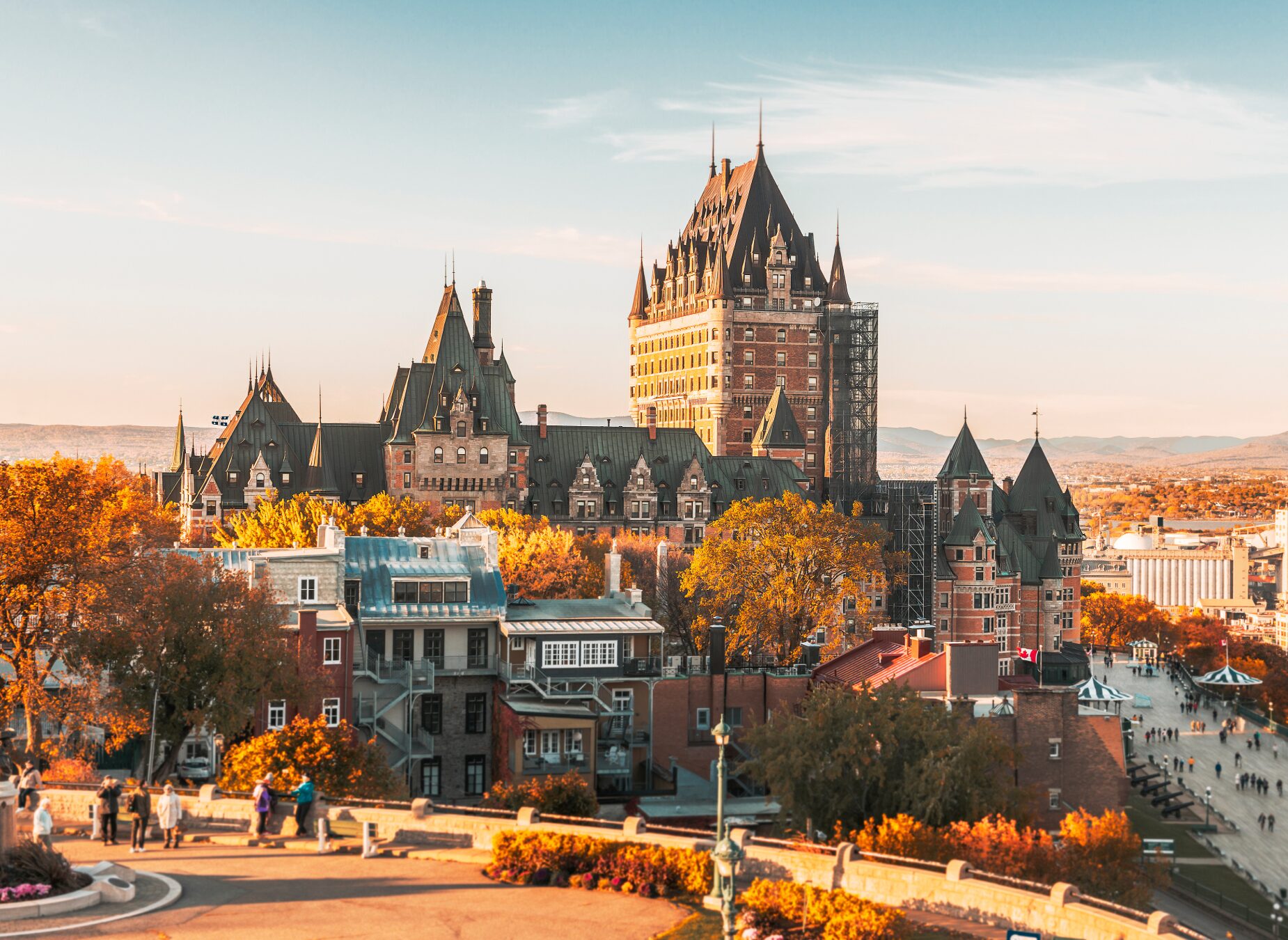 Vue du Château Frontenac à Québec, Canada, près de la route des navigateurs à vélo, entouré de feuillages d'automne et de bâtiments historiques sous un ciel dégagé. On peut voir des personnes marchant au premier plan. - Ekilib