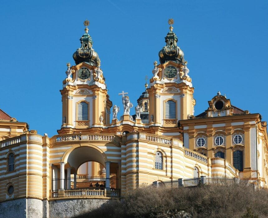 Gros plan sur la façade jaune et blanche de l'abbaye de Melk, en Autriche, l'un des points forts de la route cycliste Danube Passau Vienne, avec ses deux tours, ses fenêtres cintrées, ses statues et ses détails baroques, le tout dans un ciel bleu limpide. - Ekilib