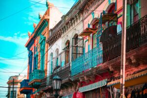 Une rangée de bâtiments colorés avec des balcons et des auvents ornés borde une rue sous un ciel bleu en Argentine. Des fils électriques traversent la scène, un lampadaire se dresse au premier plan, capturant l'esprit d'un voyage à vélo à travers des paysages urbains vibrants. - Ekilib