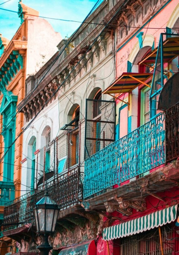 Une rangée de bâtiments colorés avec des balcons et des auvents ornés borde une rue sous un ciel bleu en Argentine. Des fils électriques traversent la scène, un lampadaire se dresse au premier plan, capturant l'esprit d'un voyage à vélo à travers des paysages urbains vibrants. - Ekilib